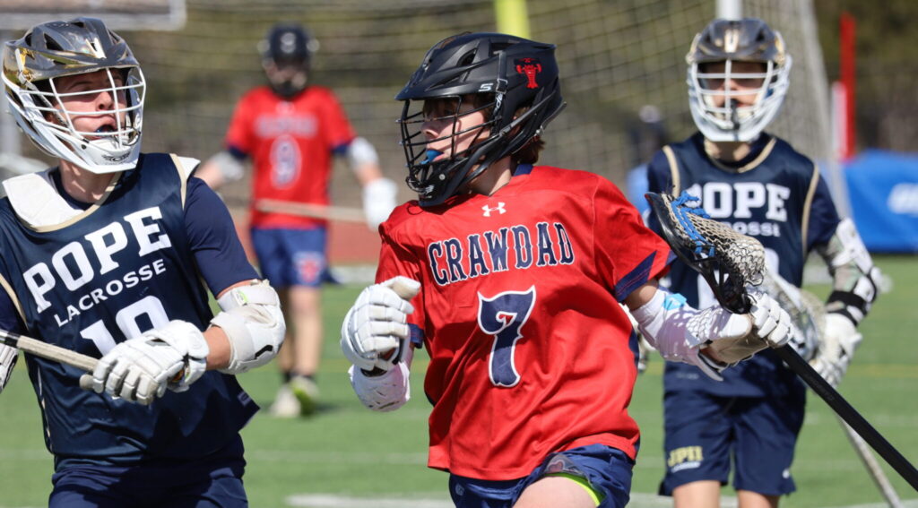 Crawdads youth lacrosse player in red jersey driving the ball past defenders from Pope Lacrosse during a game.